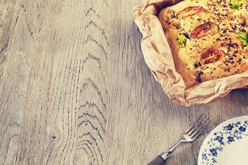 Vintage toned traditional Italian focaccia with tomatoes on an old wooden table, space for text.