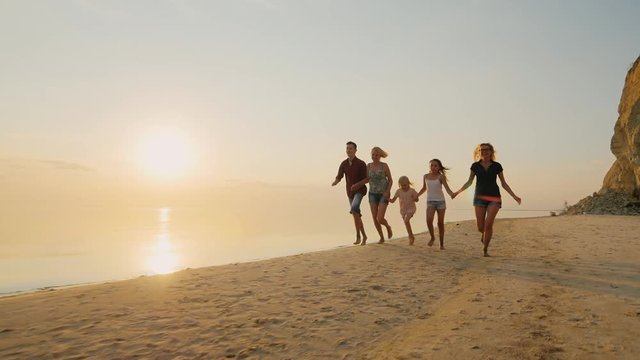 Group of carefree children of different ages and adults have fun running on the beach at sunset