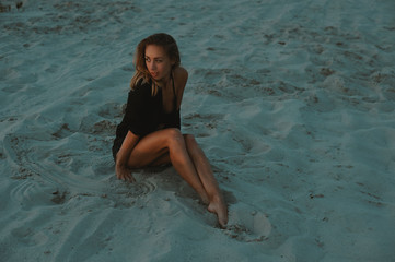 sexy blonde haired young woman posing in sands of desert lit by red setting sun light