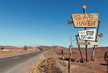 Tuinposter Deserted road  and tall vintage gas sign  in typical Moroccan landscape near Ouarzazate,  Morocco. © Antonel