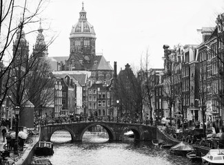 The Oudezijds Voorburgwal a street and canal in the Red-light district in the center of Amsterdam. In the background Basilica of St. Nicholas. Black and white
