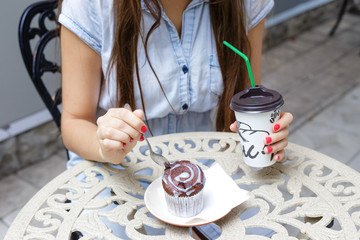 Fototapeta na wymiar Young woman eating muffin and drink coffee in outdoors cafe