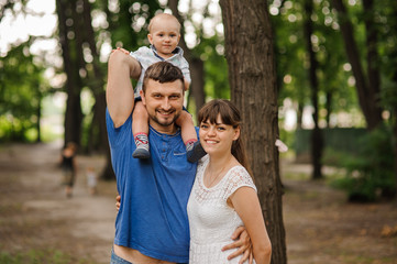 Fototapeta premium Happy family of three. Father keeps son on shoulders. Concept relations and carefree leisure time