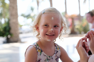 kleines blondes Mädchen beim auftragen von sonnencreme