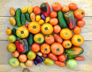 Crop of yellow and red tomatoes, cucumbers, sweet peppers on light wood surface. Top view.