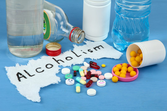 A bottle of vodka near pills and napkin with inscription "Alcoholism" on wooden background. The concept of alcoholism