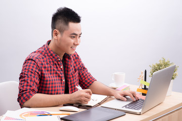 Fototapeta na wymiar Asian Man Writing At Desk In Busy Creative Office