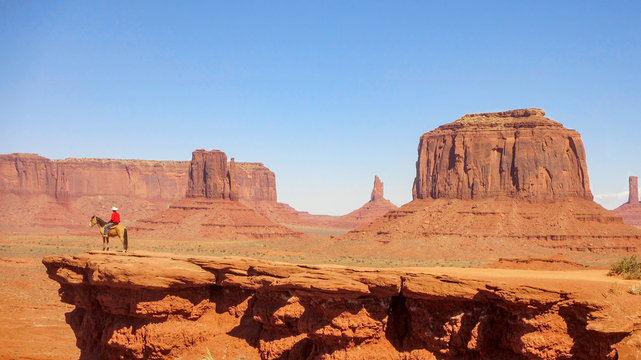 Monument Valley and a single horse rider at the end of the track at the edge of the steep cliff.