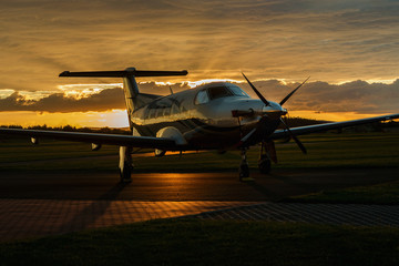 Single turboprop aircraft on runway at sunset time.