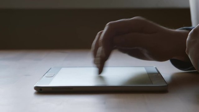 A silhouette of A hands of young man touching on a tablet PC at the table