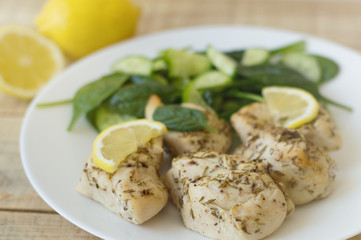Baked chicken fillet cooked with thyme and lemon. Chicken chops served with baby spinach and cucumber on a white plate
