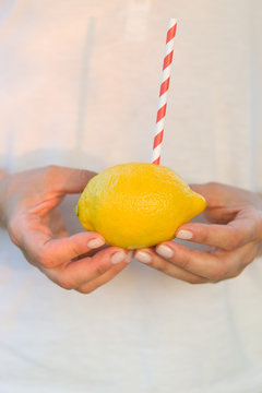 Big yellow lemon with red and white stripes straw in woman's hands. Vitamins and healthy food concept