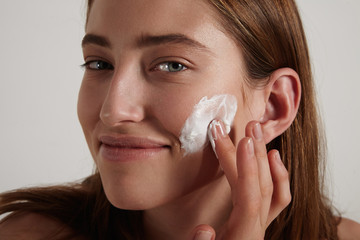 pretty young woman puts cream on cheek