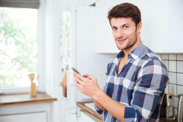Happy young man using cell phone on the kitchen