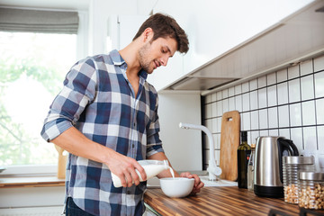 Man pouring milk into bowl for breakfast on the kitchen