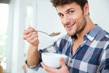 Happy young man eating cereals with milk at home