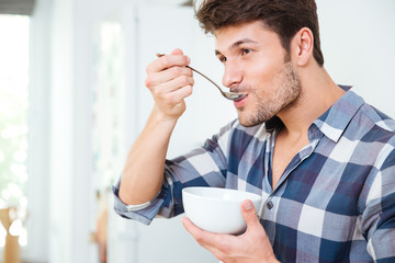 Handsome young man having breakfast at home