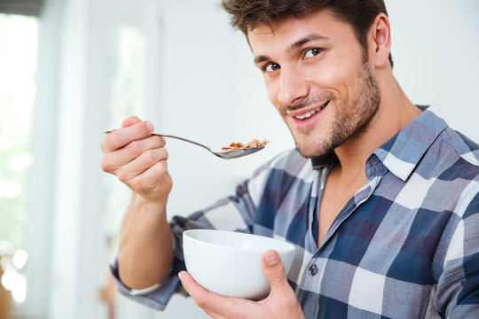 Happy young man eating cereals with milk at home