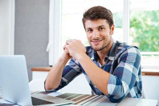 Smiling young man sitting and working with laptop at home