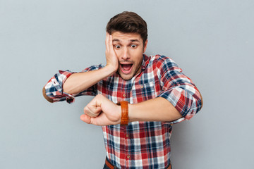 Astonished young man in checkered shirt looking at wristwatch