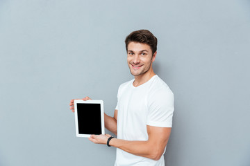 Smiling handsome young man standing and holding blank screen tablet