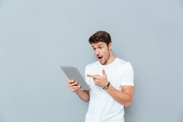 Surprised young man holding and pointing on tablet