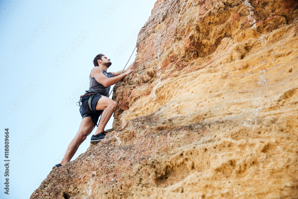 Wall mural Young man climbing natural rocky wall