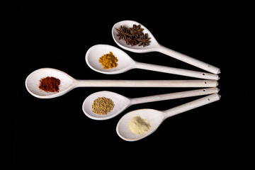 Mixture of spices on wooden kitchen spoons on a black background.
