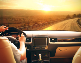 Male hands on car steering wheel. View from car windshield to road and beautiful landscape.