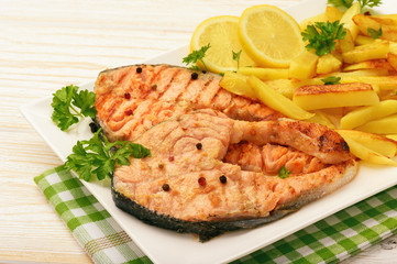 Grilled salmon with fried potatoes and slices of lemon.