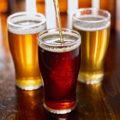 pouring beer into glass with assorted types of beers in background