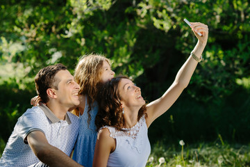 Young smiling and laughting happy family of three taking selfie in the park