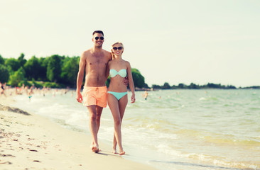 happy couple in swimwear walking on summer beach