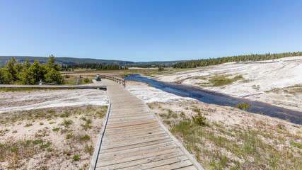 Fototapeta premium Colorful landscapes of geothermal activity. Wooden walkway among the geysers. Old Faithful Geyser, Yellowstone National Park, Wyoming, USA