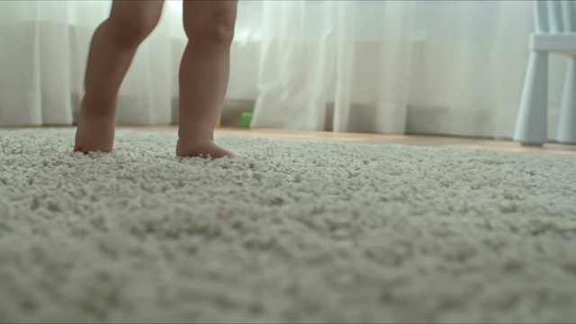 Closeup of barefoot legs of little child walking by herself on the carpet in the kids room