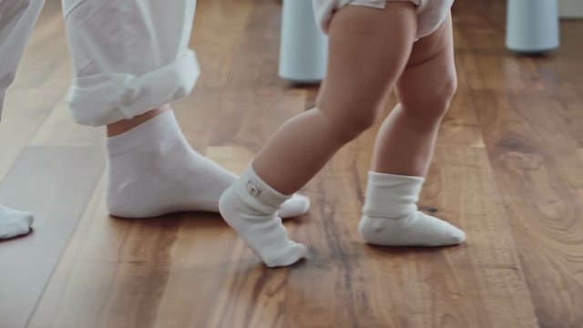 Side view of legs of woman walking behind little baby in white socks in slow motion