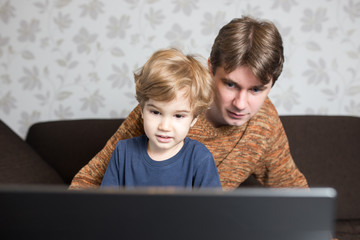 Father and son using laptop together on sofa at home