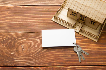 Real Estate Concept. Model house, keys, blank business card on wooden table. Top view. Toned image