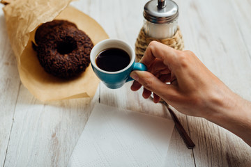 Man hands eating chocolate donut with coffee on wooden table