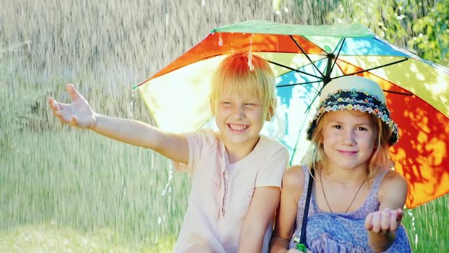 Two cheerful girlfriends 5 years hiding from the rain under an umbrella rainbow colors. Happy childhood, friendship