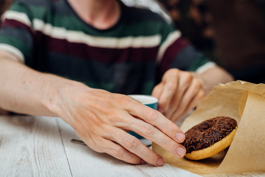 Man hands eating chocolate donut with coffee on wooden table