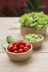 Fresh cherry tomato in round wooden bowl with fresh cucumber and lettuce, salad concept, healthy lifestyle
