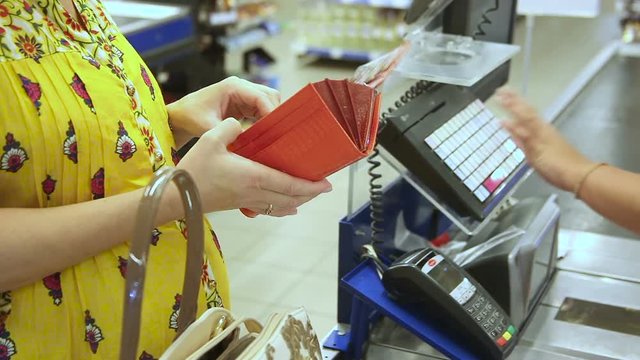 Pregnant woman gets money from her purse to calculate for goods purchased in the supermarket.