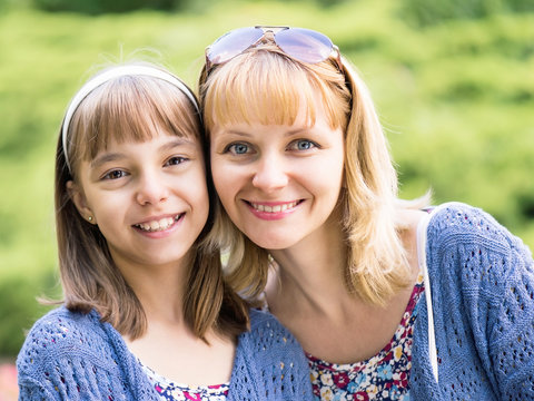 Happy family outdoors in summer day. Mother Day. Portrait of mother and daughter smiling into the camera lens. Woman with child having fun together during walk in the park.