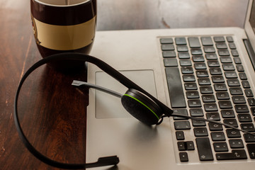 Headset, Kaffeetasse und Laptop auf Holztisch