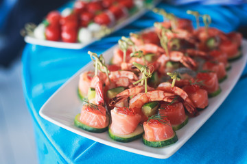 Beautifully decorated catering banquet table with different food snacks and appetizers with sandwich, caviar, fresh fruits on corporate open-air party event or wedding celebration