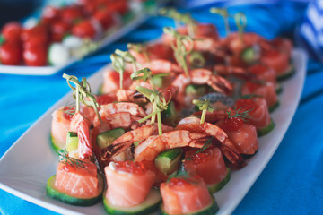 Beautifully decorated catering banquet table with different food snacks and appetizers with sandwich, caviar, fresh fruits on corporate open-air party event or wedding celebration