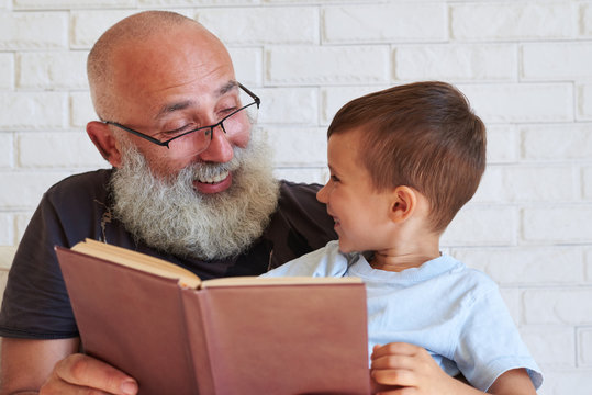 Close-up of aged man and small boy with a book looking at each o