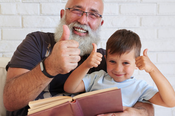 Portrait of aged man and small boy sitting in armchair with a bo