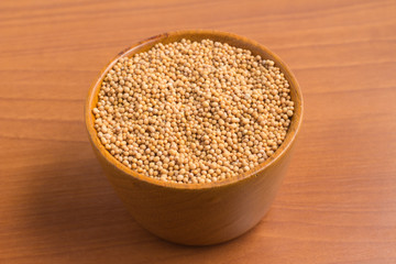 Mustard seeds into a bowl over a wooden table